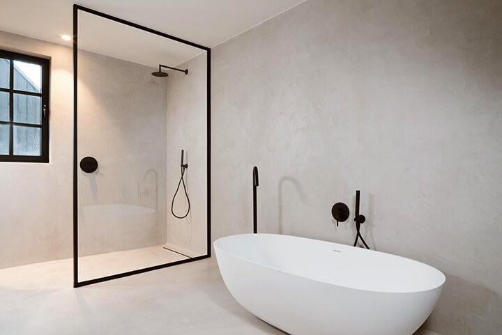 badkamer met wit vrijstaand bad zwart douchescherm en mortex vloeren en muren
